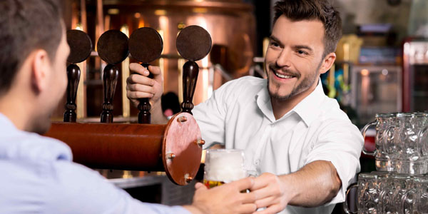 bartenders A male bartender with his hand on a beer tap and passing a pint to a customer